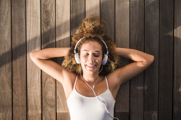 Portrait of young woman with eyes closed lying on wooden floor listening music with headphones - SIPF01062