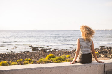 Back view of woman sitting on a wall looking at the sea - SIPF01064