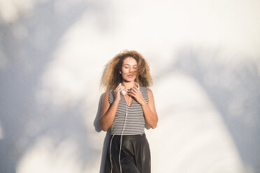 Young woman with eyes closed leaning against wall at sunlight - SIPF01067