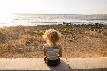 Rückenansicht einer Frau, die auf einer Mauer sitzt und auf das Meer schaut - SIPF01076