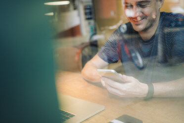 Smiling man at desk with cell phone and laptop - GIOF01596