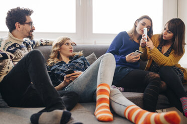 Four friends with smartphones on couch in living room hanging out - LCUF00076