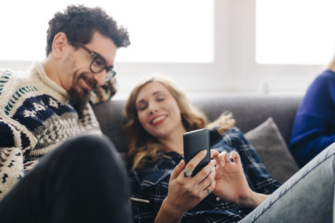 Junge Frau tauscht mit einem Freund im Wohnzimmer Nachrichten auf dem Smartphone aus, lizenzfreies Stockfoto