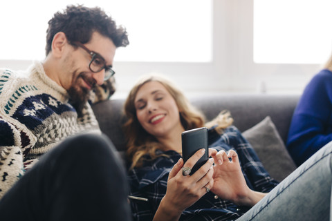 Young woman sharing message on smartphone with friend in living room stock photo