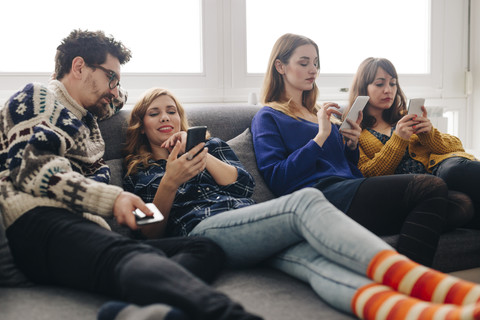 Four friends with smartphones on couch in living room hanging out stock photo