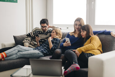 Four friends with smartphones on couch in living room hanging out - LCUF00082