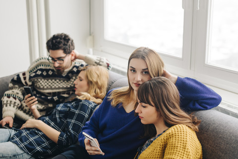 Vier Freunde mit Smartphones auf der Couch im Wohnzimmer hängen ab, lizenzfreies Stockfoto