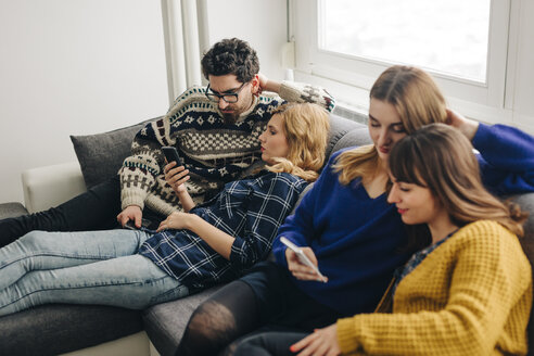 Four friends with smartphones on couch in living room hanging out - LCUF00084