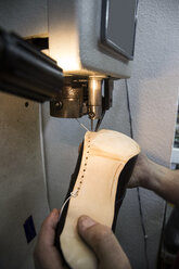 Shoemaker sewing the sole of a shoe using a machine in his workshop - ABZF01473