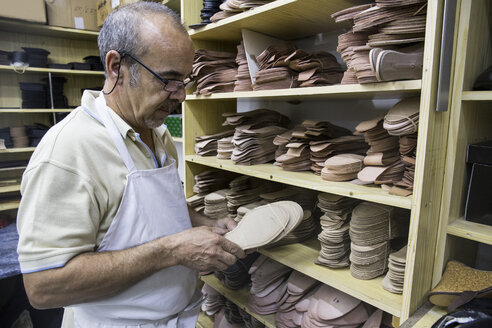 Schuhmacher beim Aussuchen von Schuhsohlen aus einem Regal in seiner Werkstatt - ABZF01482