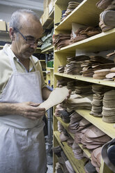 Schuhmacher beim Aussuchen von Schuhsohlen aus einem Regal in seiner Werkstatt - ABZF01483