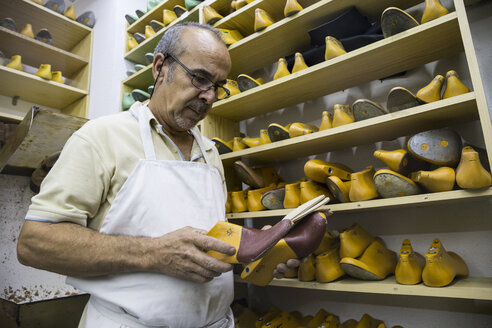 Schuhmacher wählt Schuhleisten aus einem Regal in seiner Werkstatt aus - ABZF01484