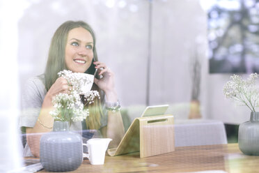 Smiling young woman at home using cell phone and tablet - MADF01180