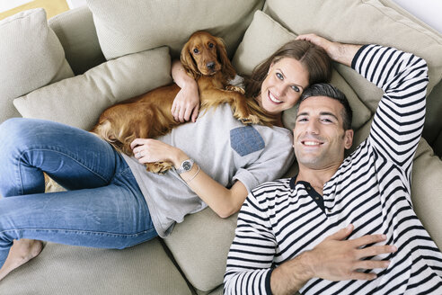 Lächelndes Paar mit Hund auf Couch liegend - MADF01198