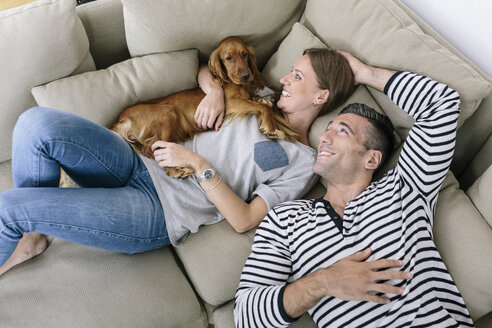 Lächelndes Paar mit Hund auf Couch liegend - MADF01199