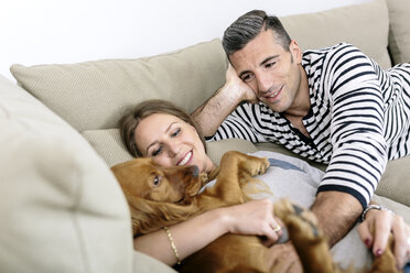 Lächelndes Paar mit Hund auf Couch liegend - MADF01200
