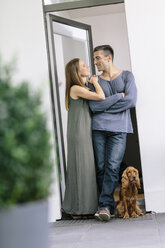 Smiling couple with dog standing at terrace door - MADF01204