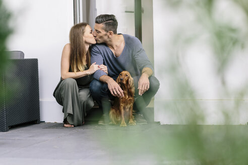 Pärchen mit Hund küsst sich an der Terrassentür - MADF01205
