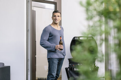Lächelnder Mann mit Bierflasche vor der Terrassentür - MADF01209