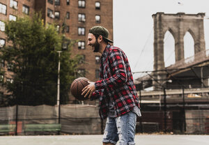 USA, New York, lachender junger Mann mit Basketball auf einem Platz im Freien - UUF09125