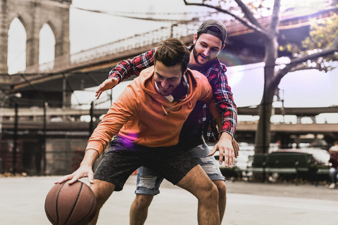 USA, New York, zwei junge Männer spielen Basketball auf einem Platz im Freien, lizenzfreies Stockfoto