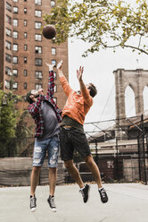 USA, New York, zwei junge Männer spielen Basketball auf einem Platz im Freien - UUF09127