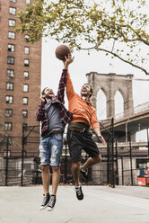 USA, New York, zwei junge Männer spielen Basketball auf einem Platz im Freien - UUF09128