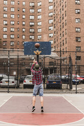 Junger Mann spielt Basketball auf einem Platz im Freien - UUF09129