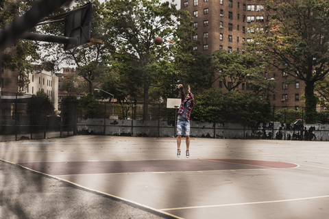 Junger Mann spielt Basketball auf einem Platz im Freien, lizenzfreies Stockfoto