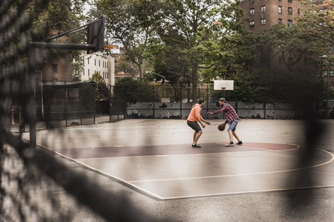 Zwei junge Männer spielen Basketball auf einem Platz im Freien, lizenzfreies Stockfoto