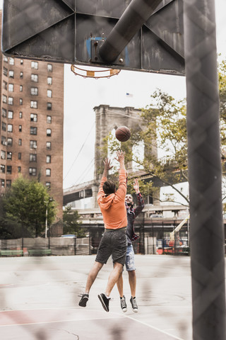 USA, New York, zwei junge Männer spielen Basketball auf einem Platz im Freien, lizenzfreies Stockfoto