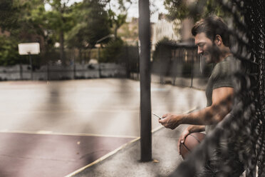 Junger Mann mit Mobiltelefon und Basketball auf einem Platz im Freien - UUF09137