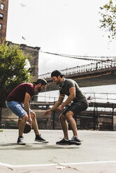 USA, New York, zwei junge Männer spielen Basketball auf einem Platz im Freien - UUF09149