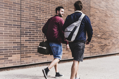 Zwei Freunde mit Taschen gehen auf dem Bürgersteig, lizenzfreies Stockfoto