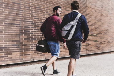 Zwei Freunde mit Taschen gehen auf dem Bürgersteig - UUF09156