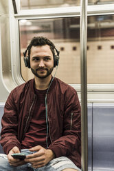 Junger Mann sitzt in der U-Bahn und trägt Kopfhörer - UUF09157