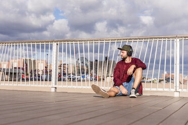 USA, New York City, Mann sitzt auf einer Brücke auf Coney Island und trägt Kopfhörer - UUF09165