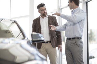 Car dealer talking to client in showroom - ZEF11528