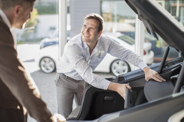 Car dealer opening hatchback of car to customer at car dealership - ZEF11533