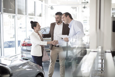 Car dealer shaking hands with woman in car dealership - ZEF11536