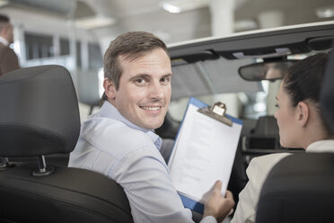 Smiling car dealer with clipboard and woman in car - ZEF11543