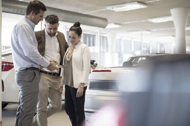 Car dealer talking to couple in showroom - ZEF11548