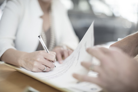 Frau unterschreibt Vertrag am Schreibtisch im Autohaus, lizenzfreies Stockfoto