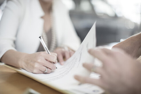 Woman signing contract at desk at car dealership - ZEF11554