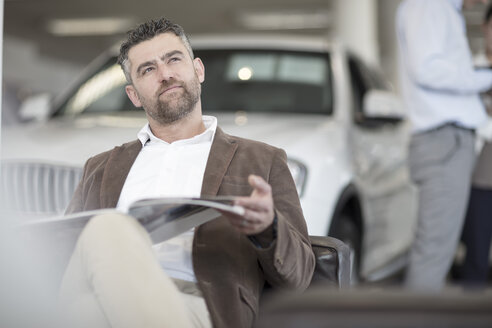 Man sitting with magazine at car dealership - ZEF11558