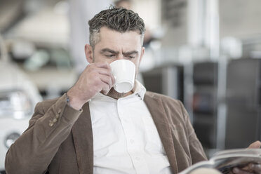 Man drinking coffee reading magazine at car dealership - ZEF11559