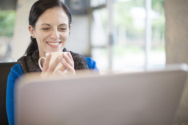 Smiling woman at desk with coffee cup and laptop - ZEF11579