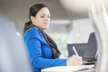 Frau am Schreibtisch mit Laptop, die in ein Notizbuch schreibt - ZEF11580