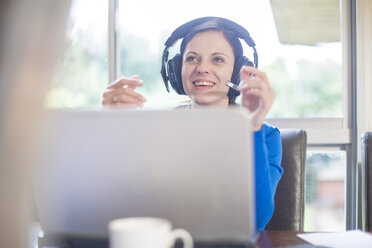 Smiling woman at desk with laptop and headset - ZEF11581