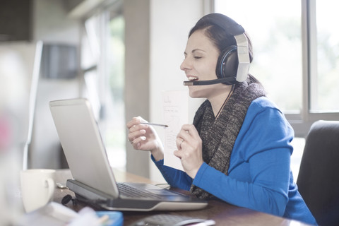 Smiling woman at desk with laptop and headset stock photo